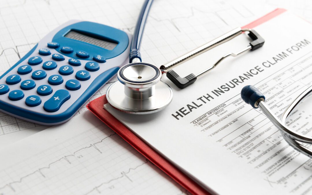 Calculator, stethoscope, and health insurance claim form on a clipboard, symbolizing medical costs.