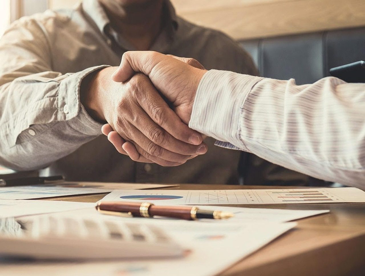 Two people shaking hands over a table with Medicare documents representing a successful Medicare plan consultation and agreement.