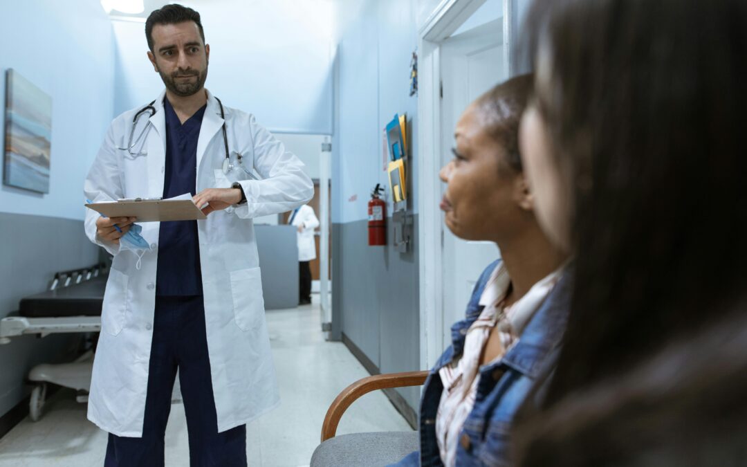 A doctor in white scrubs, reading reports in front of a woman in blue denim.