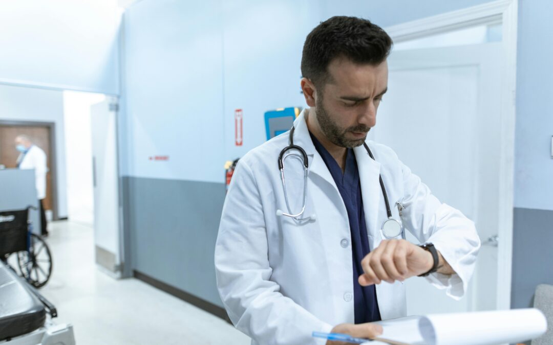 A doctor in a white lab coat holding a clipboard while talking to a patient in a clinic hallway