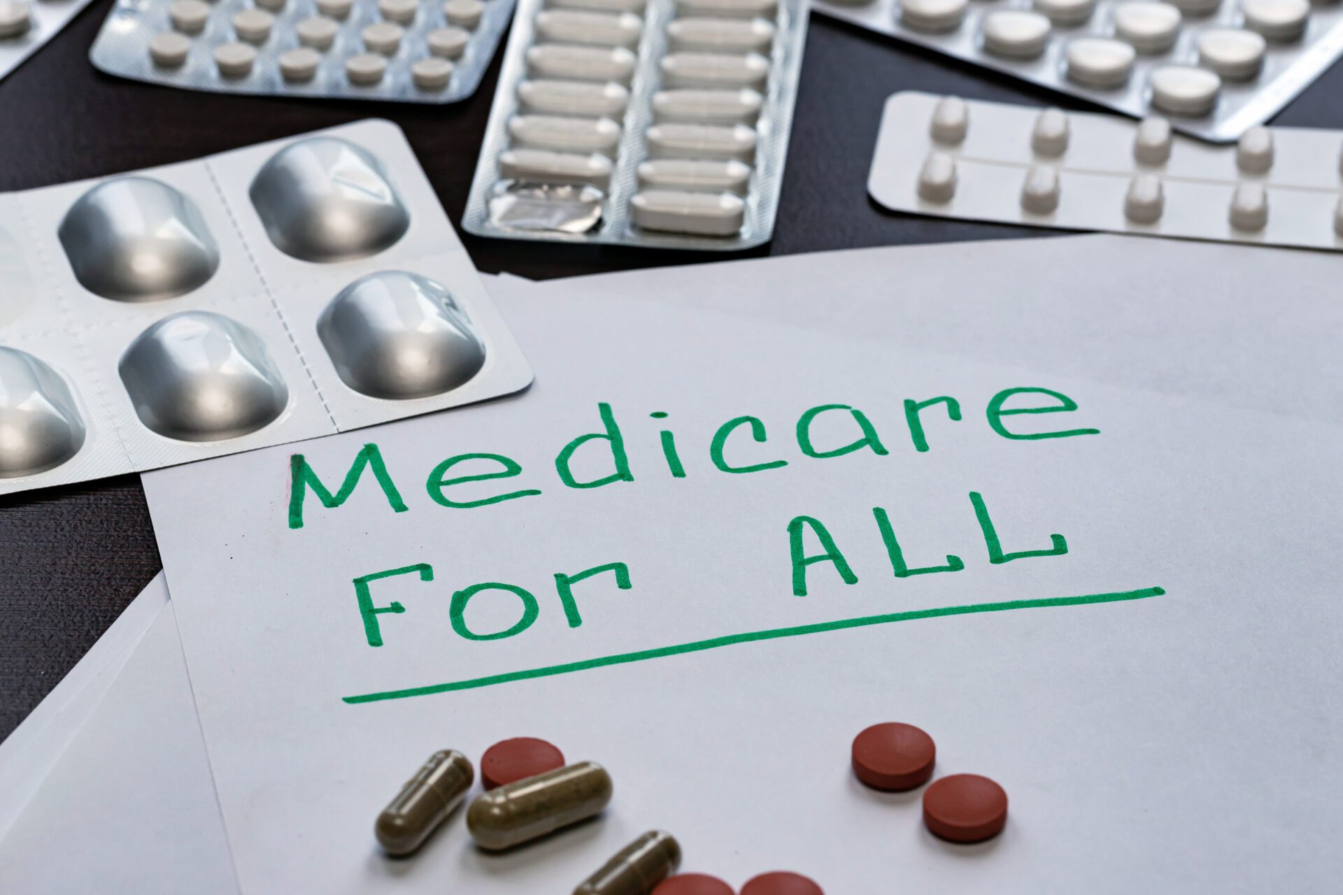 Image of ‘Medicare for all’ sign is written on the sheet in green letters, next to the pills.